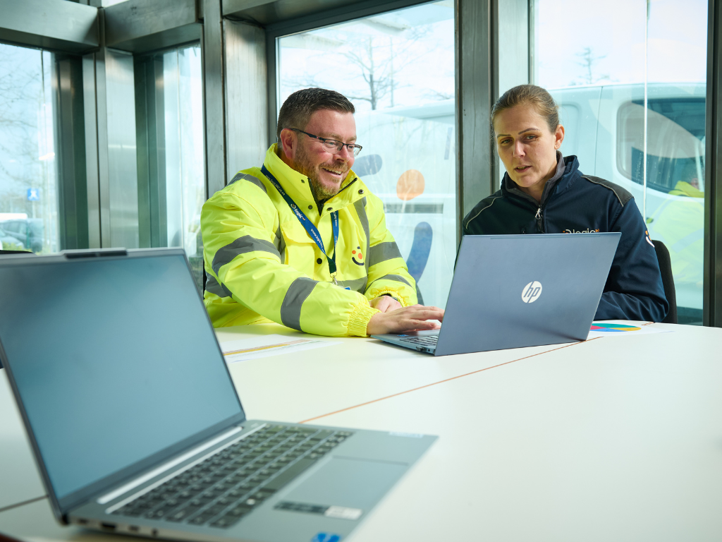 A Logic 360 operative in a hi-vis jacket working through data on a laptop with a colleague.