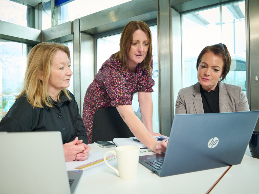 Three Logic 360 colleagues reviewing performance figures on a laptop in a meeting room.